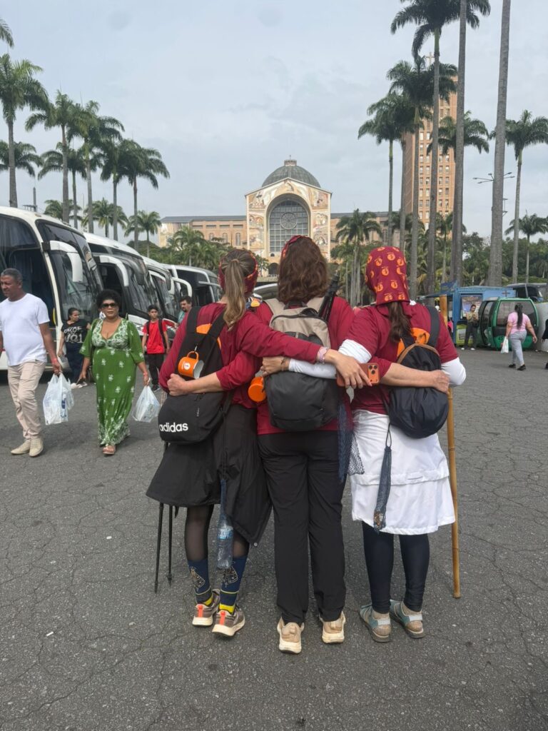 Três peregrinas abraçadas olhando a Basílica de Aparecida